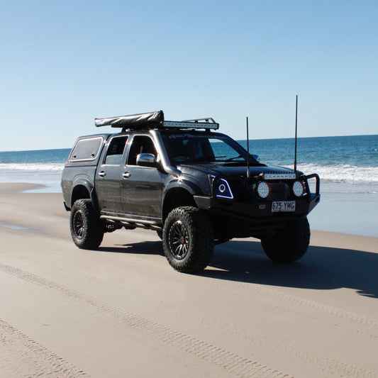 A black modififed 4x4 driving on the beach, alongside blue waves.